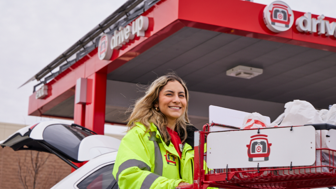 A Target team member wearing a yellow jacket smiles while pushing a cart at Drive Up.