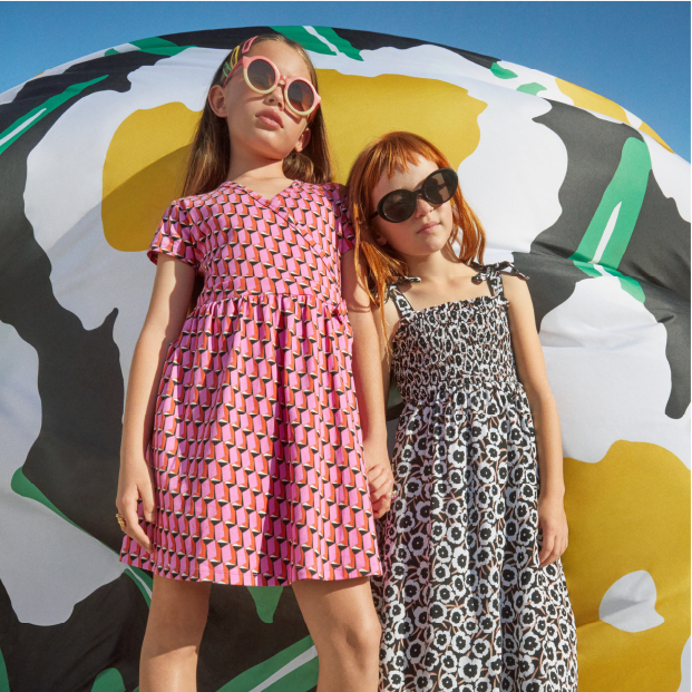 Two children pose in colorful geometric dresses.