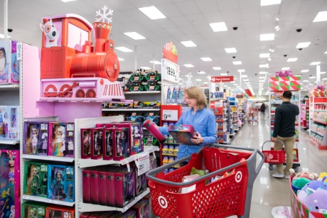 A guest in a blue sweater pushing a red cart shops for toys in Target's toy aisles.