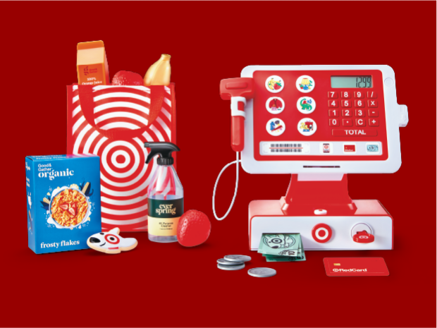 The Target Toy Cash Register with pretend money and credit card, next to a Target shopping bag with pretend groceries.