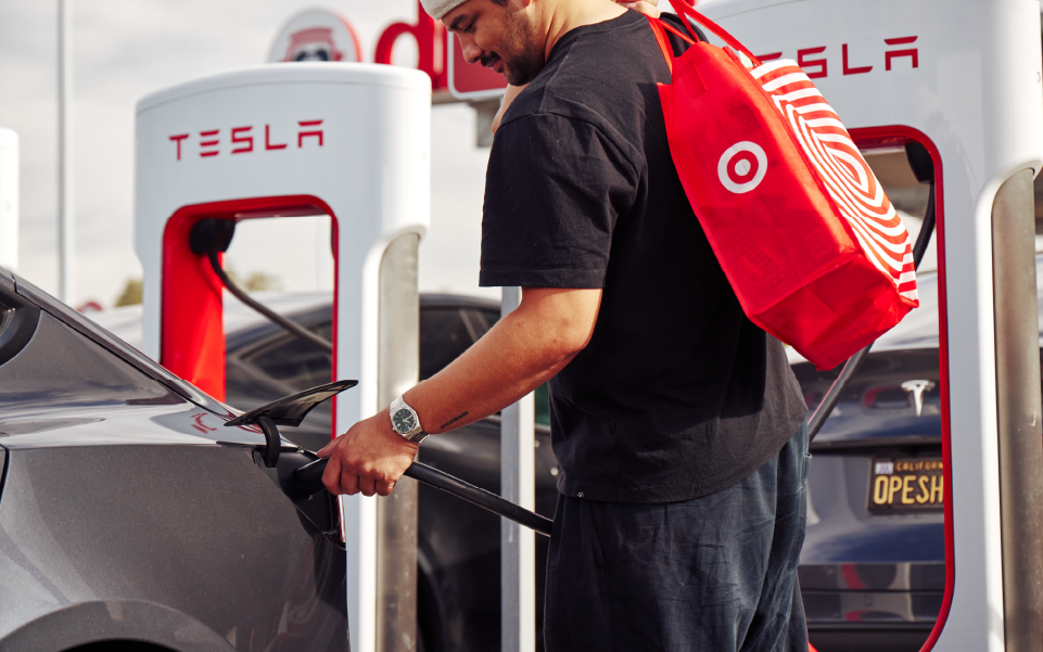 A guest holding a Target bag plugs a Tesla charger into his electric vehicle.