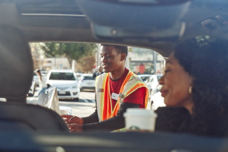 A Target team member stands outside a car window while a guest, smiling, sits inside the car.