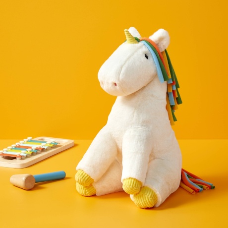 A white background displays a cream unicorn stuffed animal with a rainbow mane and a yellow horn and hooves.