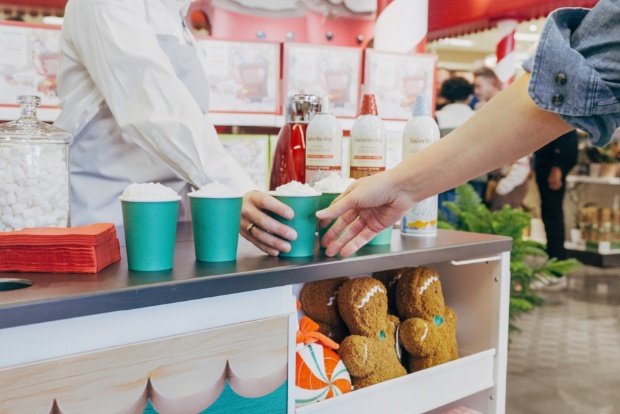 Close-up of cocoa cups being served at a festive sampling station with toppings and décor.
