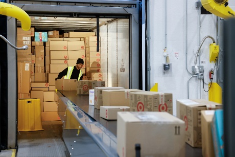 A team member wearing a hat and vest picks up boxes from a conveyor to load into a trailer.