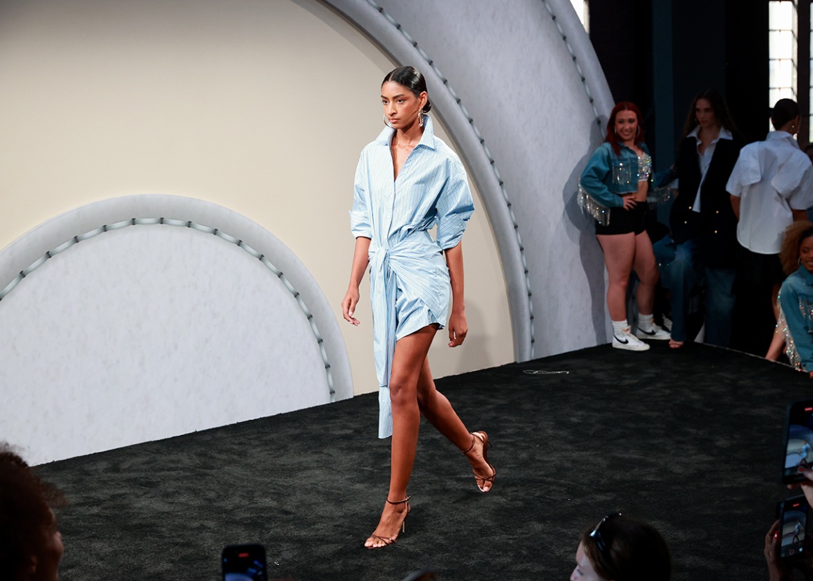 A model on a runway wears an asymmetrical blue dress