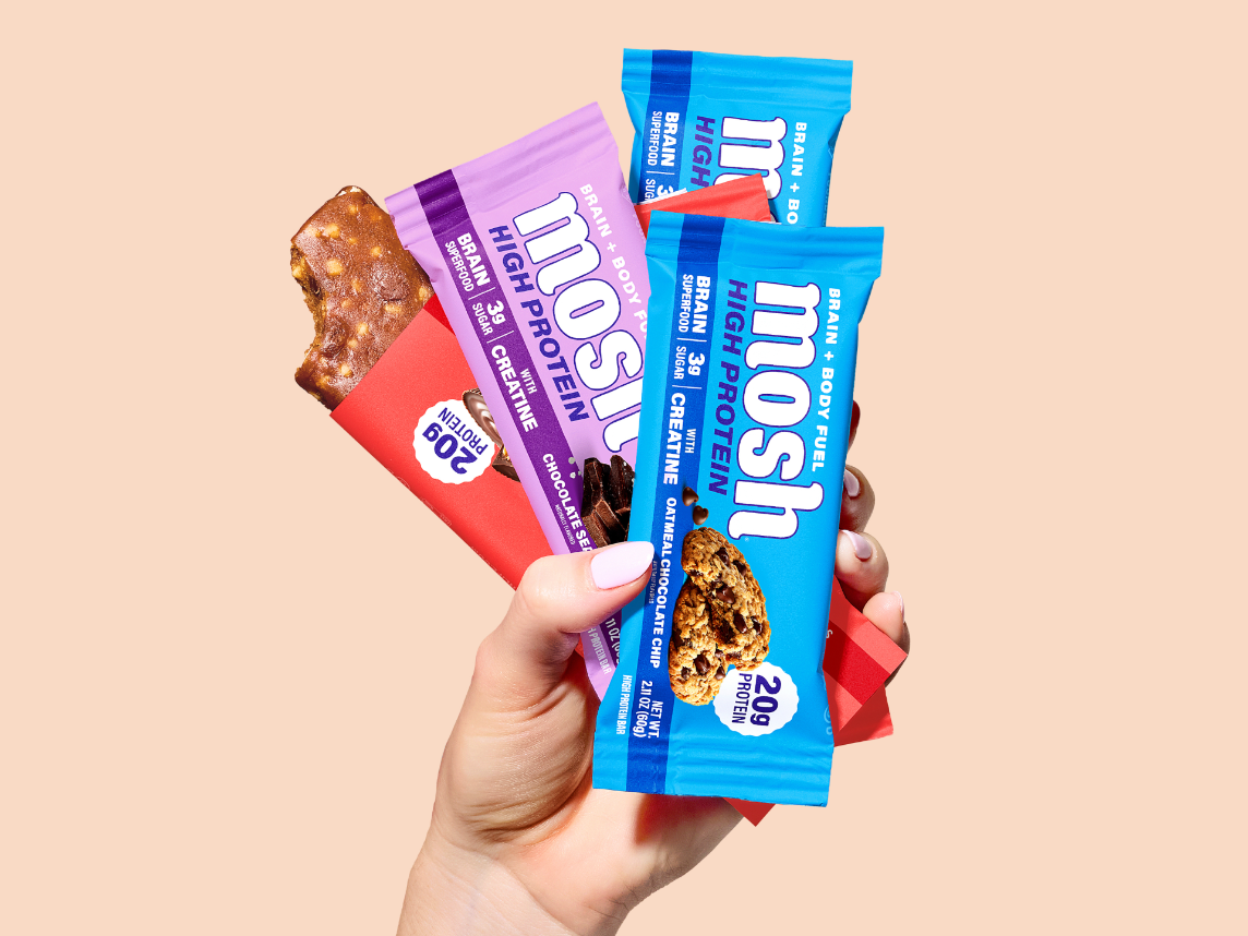 A hand holds three flavors of MOSH High Protein Bars.