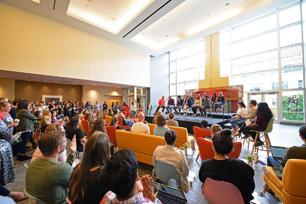 a group of people sitting in a room with a stage and a large window