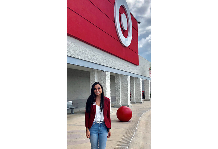 Karina stands outside her Target store wearing a red jacket, white shirt and blue jeans