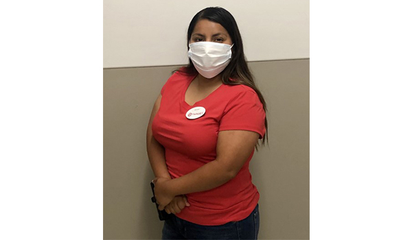 Javvi stands in her Target breakroom wearing red, khaki and a name bade and face mask. She has long, black hair.