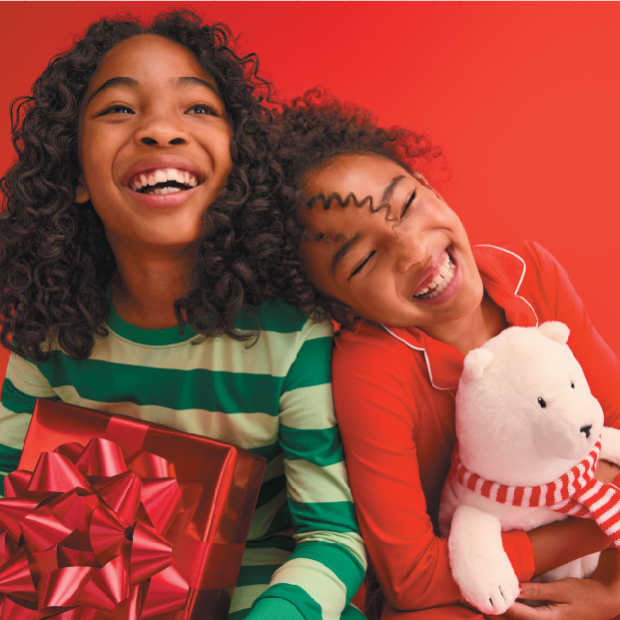 Two children smile wearing pajamas and holding holiday toys.