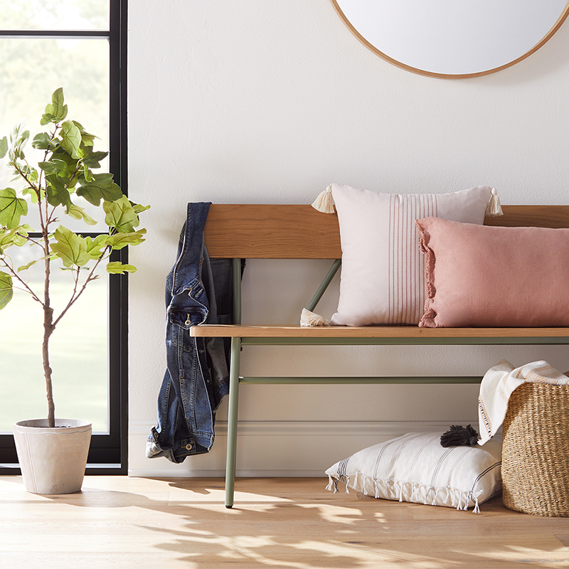 A denim jacket and neutral throw pillows adorn a wooden bench