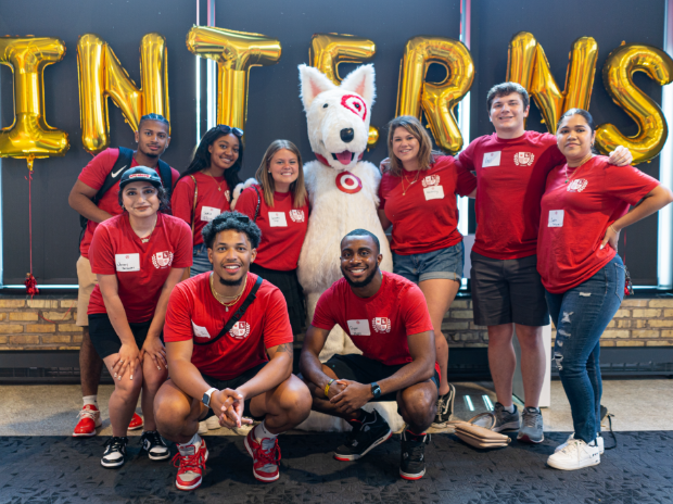 A group of interns in red shirts pose for a photo with the Bullseye mascot.