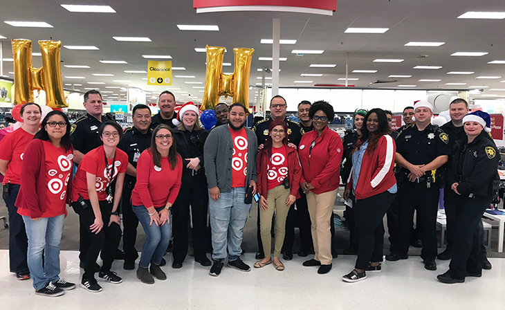 Team members in red shirts holding gold H balloons pose with their law enforcement partners in a Target aisle.