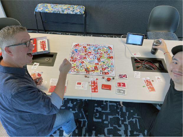 Target Associate Creative Director Ted Halbur and Senior Graphic Designer Kelvin Lee seated at a table playing The Game of Life: Target Edition.