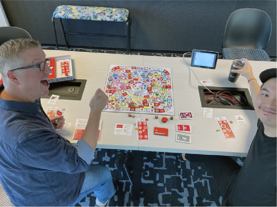 Target Associate Creative Director Ted Halbur and Senior Graphic Designer Kelvin Lee seated at a table playing The Game of Life: Target Edition.