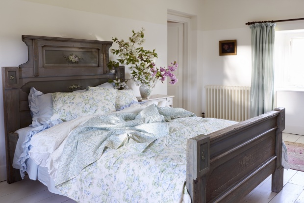 A dark wooden bed bed with a light blue floral quilt and pillows, with light blue ruffle sheets