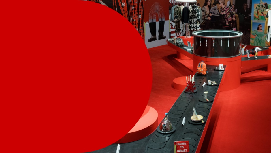Hero image with the text “Guest Experience: Inside Target’s Next Chapter of Great Design for All” beside a vivid red Target by Design exhibit at New York City’s New Museum, featuring circular display structures, a long black platform lined with curated objects, fashion imagery and colorful products throughout the space.