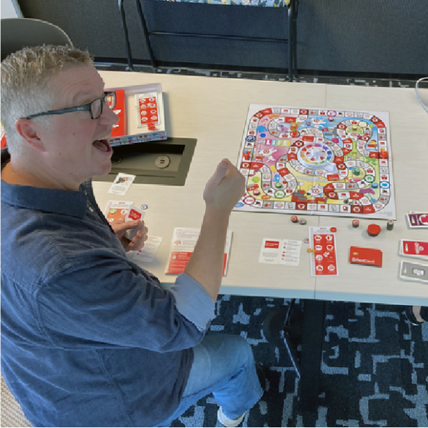 Target Associate Creative Director Ted Halbur and Senior Graphic Designer Kelvin Lee seated at a table playing The Game of Life: Target Edition.