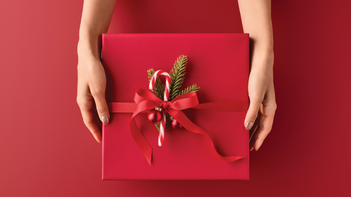 Two hands hold a gift box wrapped with a bow and candy cane.