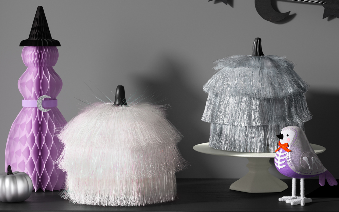 A lavender witch-shaped decoration is next to a white and a silver fringed pumpkin and a Featherly Friends bird.
