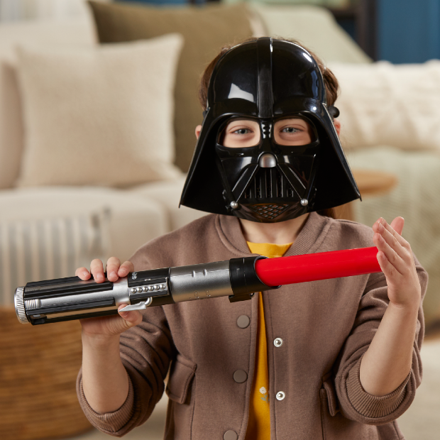 A child wears a Darth Vader mask and holds a toy lightsaber.