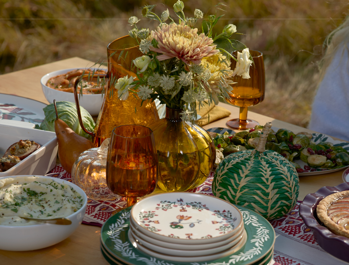 An outdoor tablescape featuring fall decor, food and dishes.