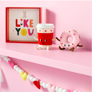 A pink shelf with a framed picture that says “I like you” next to a decorative cup of coffee and pink donut.