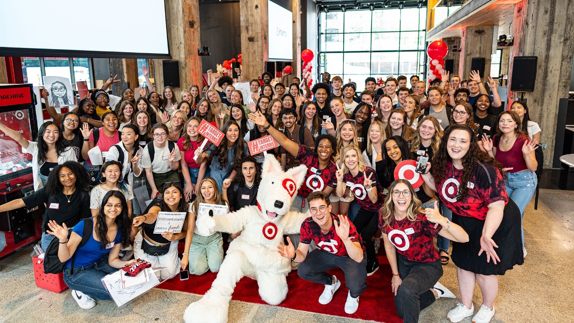 A large group Target interns pose with signs and someone dressed up as the Target Bullseye mascot at an intern event.