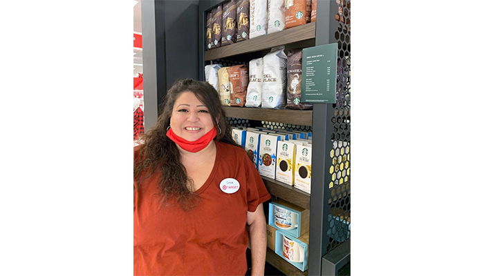 Conferina stands smiling in front of a shelf filled with coffee.