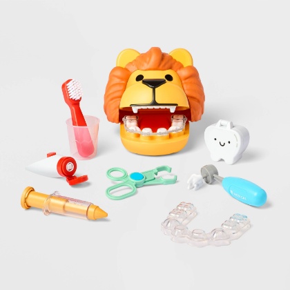 A white background displays a toothbrush in a cup, a Lion toy with big teeth and braces, floss, a retainer and other toy dentistry tools.