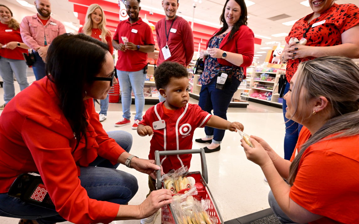 Azai hands out treats from a toy Target cart to a circle of smiling team members.