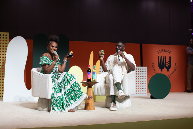 Two people sit on stage holding microphones and wine glasses.