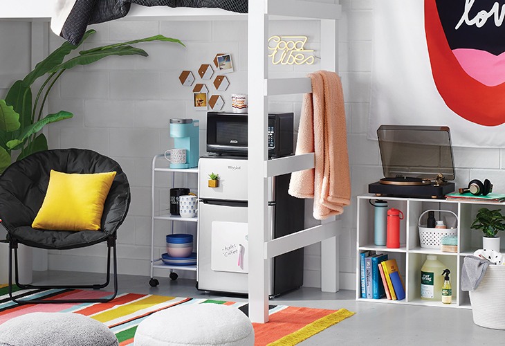A dorm room with comfy seating, fun wall decor, a fridge and microwave and a Heyday turntable