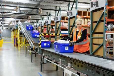 A team member wearing a vest moves a crate with guest orders on a conveyor.