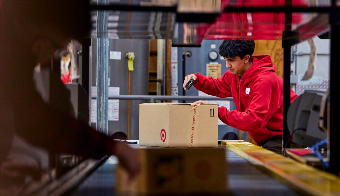 Supply chain team members guide packages down a conveyor belt.