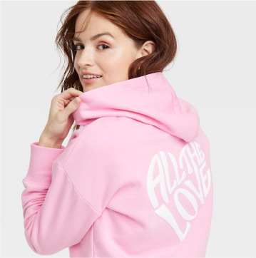 A model wearing a pink hoodie sweatshirt that says “All the love” in white print on the back.
