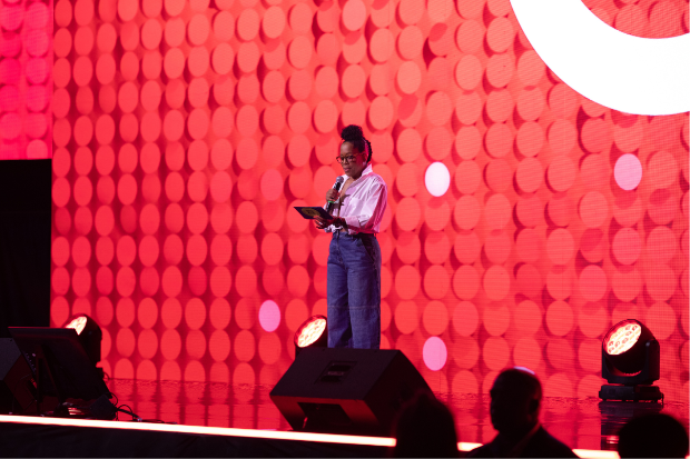 A person stands on stage holding notes and a microphone, with a Bullseye logo in the background.