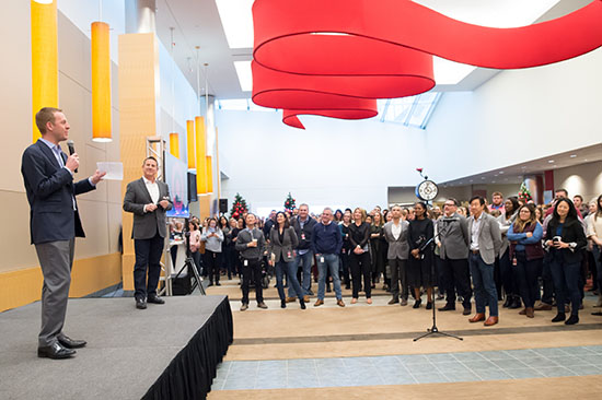 Bill and Brian stand onstage speaking in front of a crowd of team members in Target Hall