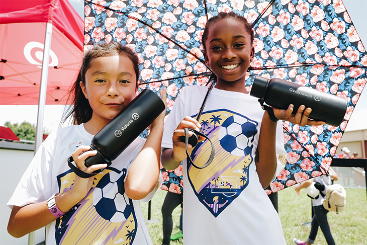 Two teen girls holding a floral umbrella and two black water bottles