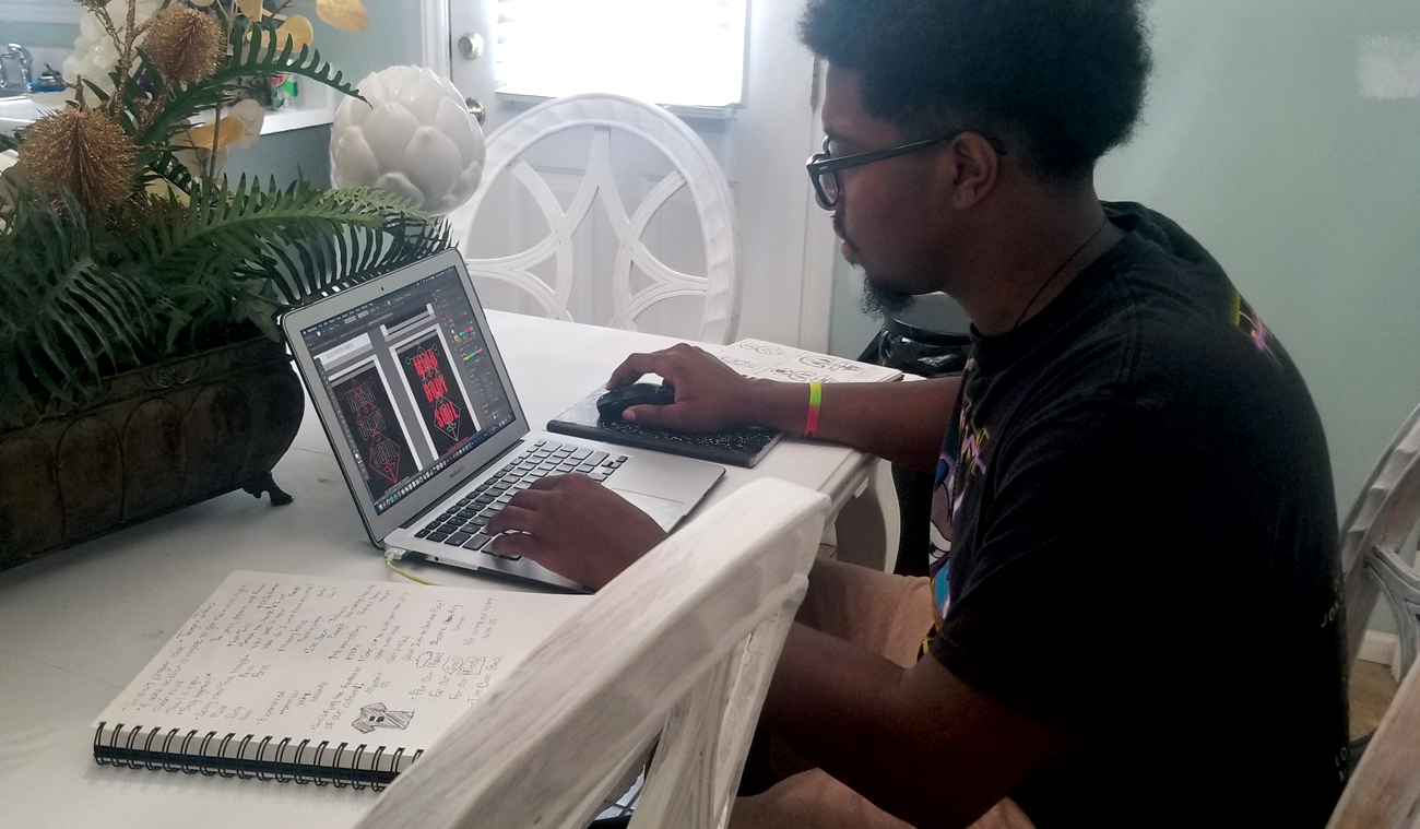 KeShawn sits at a table and works on his design at his laptop.