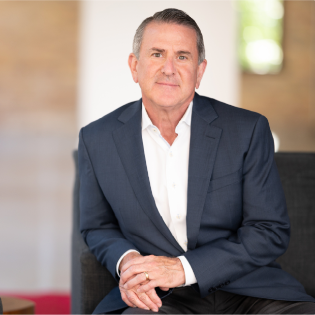 Brian Cornell sitting on a couch next to a table with a plant.