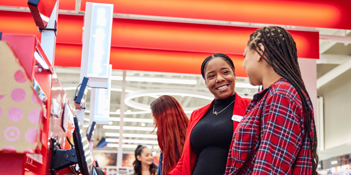 A person stands at a Target store checkout. They are wearing a team member name badge and are smiling at another person.
