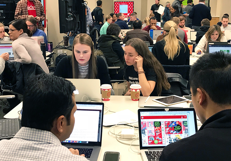 A roomful of team members sitting at tables and monitoring laptops and larger screens