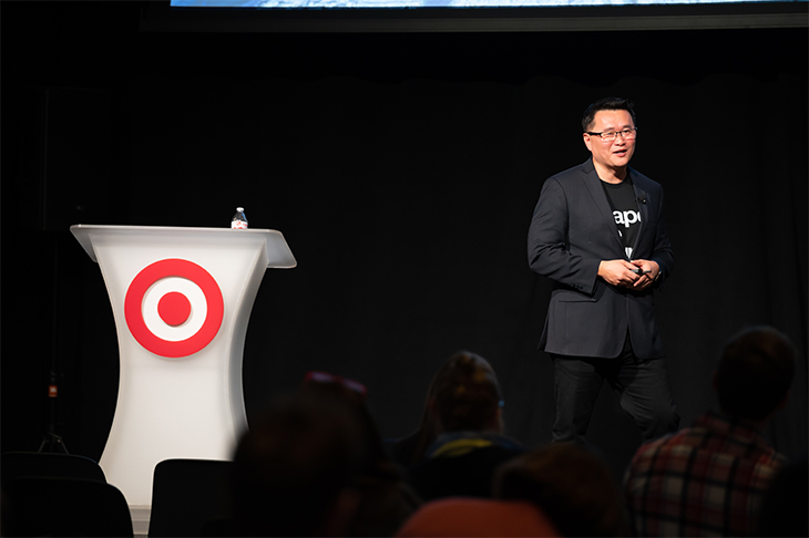 Gene stands onstage in a black jacket and tee next to a white podium with red Bullseye logo