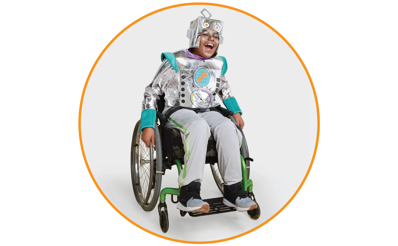 Elijah models a silver robot costume while smiling in his wheelchair