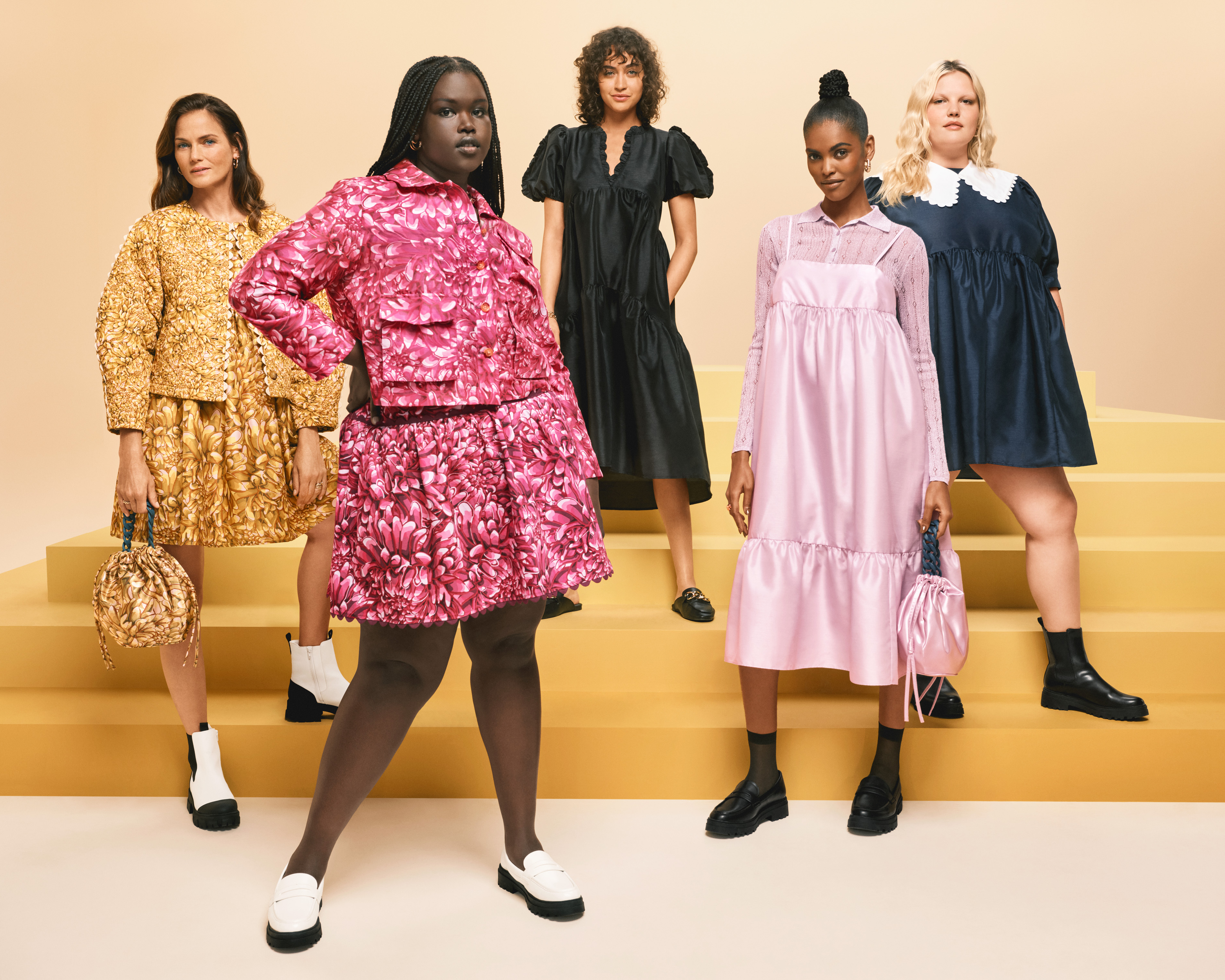 Five models stand on yellow steps wearing patterned skirts and tops and dresses.
