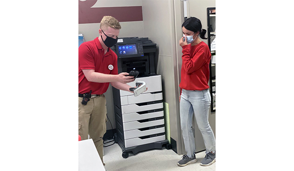 Shawn and a teammate stand in a Target backroom looking for a product together. They are both in red and khaki and wear face masks.