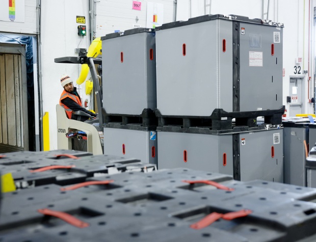 A team member driving a forklift carries four large pods.