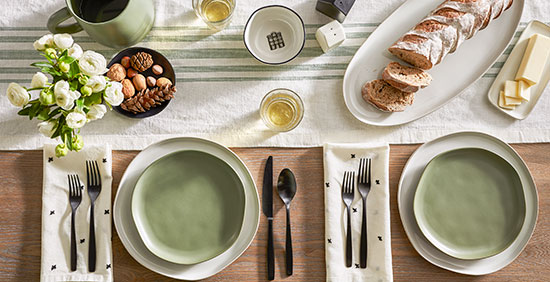 A table set with cream and sage green settings and copper tableware